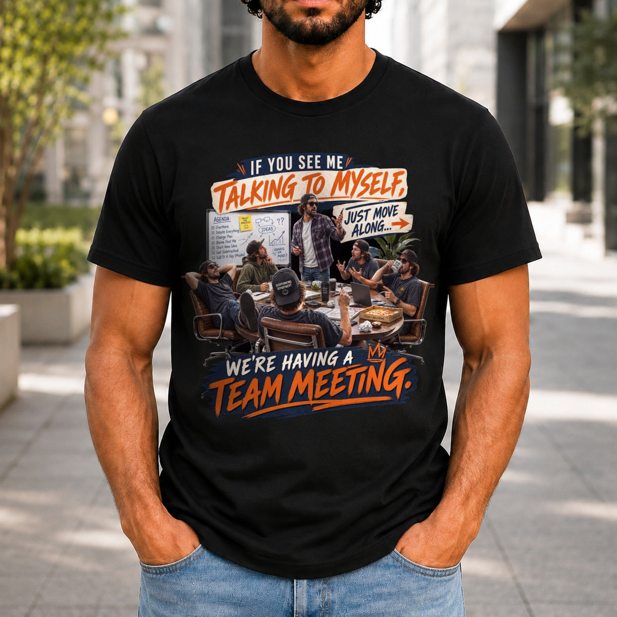We're Having A Team Meeting graphic printed on the front of a black KRED Threads premium tee