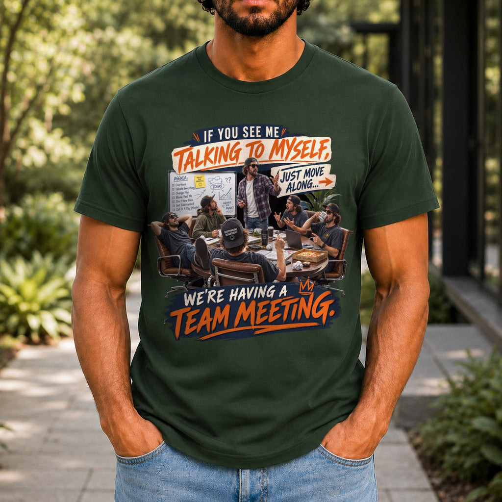 We're Having A Team Meeting graphic printed on the front of a forest green KRED Threads premium tee